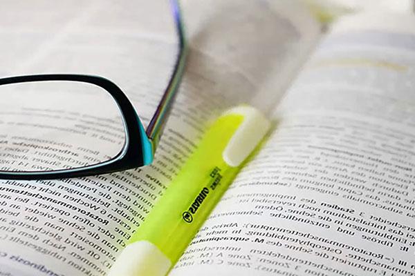 Book opened with yellow highlighter marker and reading glasses placed on top